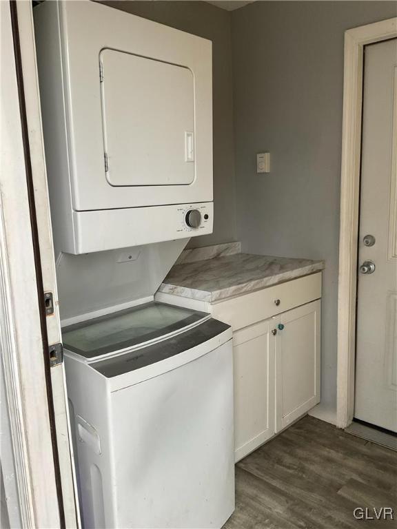 laundry area featuring cabinet space, dark wood-style flooring, and stacked washer and clothes dryer