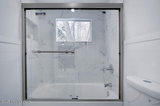 bathroom with toilet and shower / bath combination with glass door