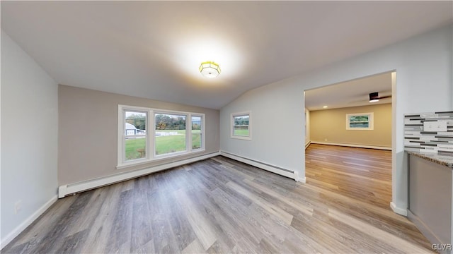 empty room featuring a baseboard radiator, vaulted ceiling, and light wood-type flooring