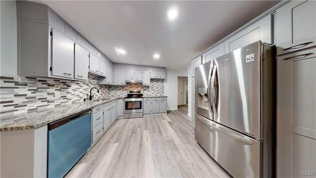 kitchen featuring appliances with stainless steel finishes, sink, decorative backsplash, light stone counters, and light wood-type flooring