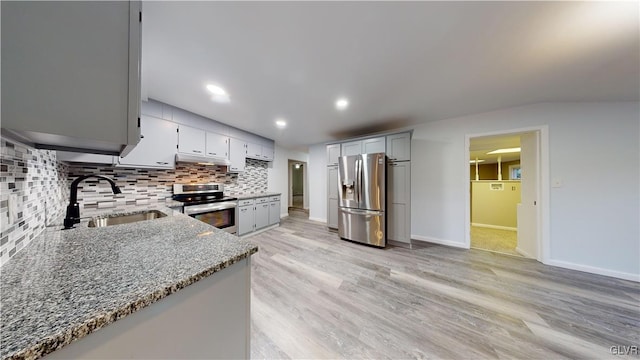 kitchen with sink, light hardwood / wood-style flooring, stone counters, appliances with stainless steel finishes, and decorative backsplash