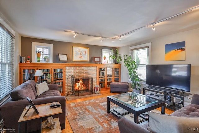 living room featuring rail lighting, a brick fireplace, and light hardwood / wood-style flooring