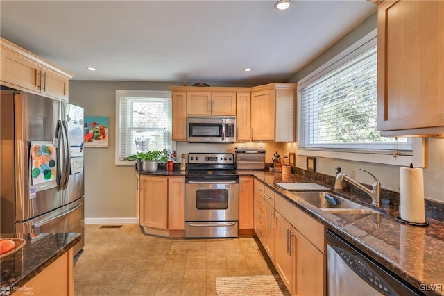 kitchen with sink, light brown cabinets, dark stone counters, and appliances with stainless steel finishes