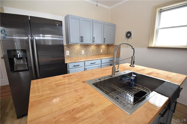 kitchen with stainless steel refrigerator with ice dispenser, sink, butcher block countertops, crown molding, and backsplash