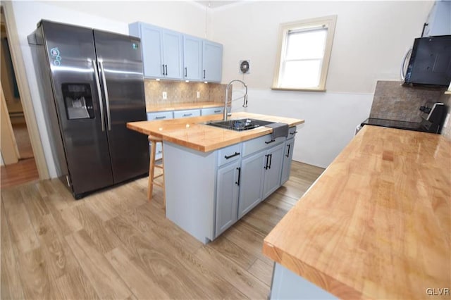 kitchen featuring appliances with stainless steel finishes, tasteful backsplash, butcher block counters, a center island with sink, and light wood-type flooring