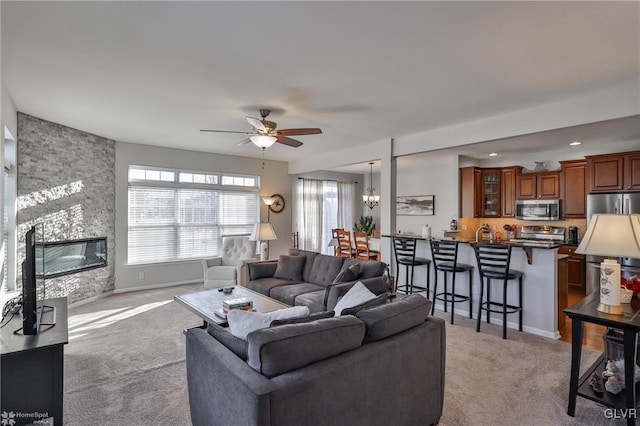 carpeted living room featuring ceiling fan with notable chandelier and a fireplace