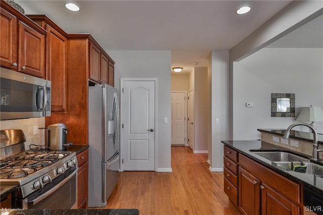 kitchen featuring sink, light hardwood / wood-style flooring, dark stone counters, and appliances with stainless steel finishes