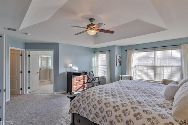 carpeted bedroom with a tray ceiling, ensuite bath, and ceiling fan