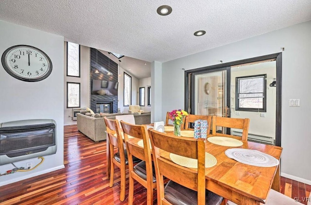 dining area featuring dark wood-type flooring, a large fireplace, a textured ceiling, and baseboard heating