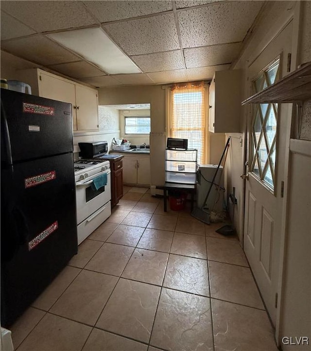 kitchen with light tile patterned floors, a paneled ceiling, white gas stove, and black fridge