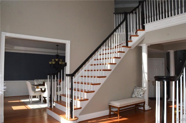 stairway with wood-type flooring, a chandelier, and decorative columns