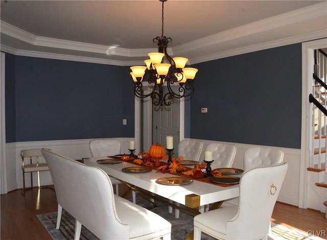 dining room with crown molding, wood-type flooring, a raised ceiling, and a chandelier