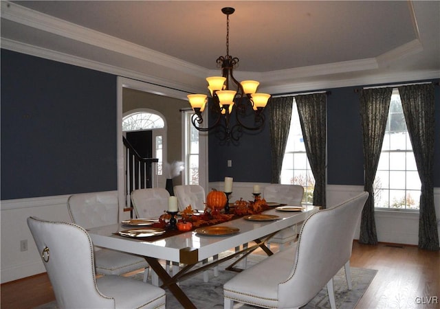 dining area featuring an inviting chandelier, ornamental molding, a raised ceiling, and hardwood / wood-style floors