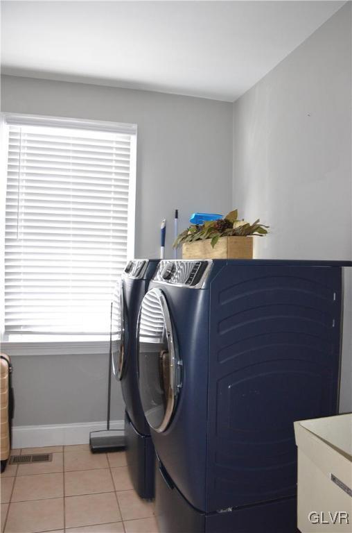 laundry area with light tile patterned floors, washer and clothes dryer, and a healthy amount of sunlight