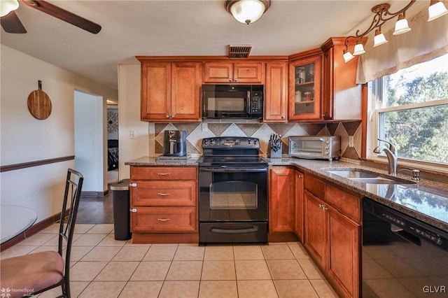 kitchen featuring sink, dark stone countertops, decorative backsplash, light tile patterned floors, and black appliances