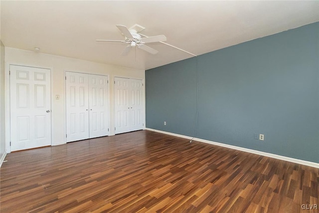 unfurnished bedroom featuring dark hardwood / wood-style flooring, two closets, and ceiling fan