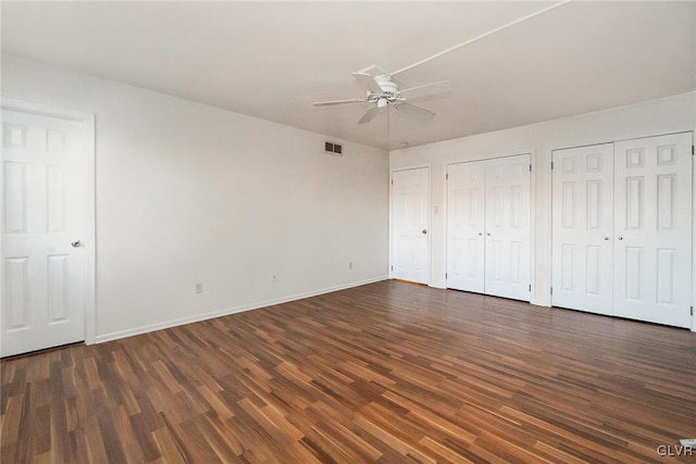 unfurnished bedroom with multiple closets, ceiling fan, and dark hardwood / wood-style flooring