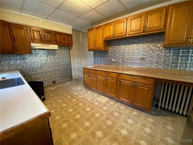 kitchen with sink, radiator, built in desk, a drop ceiling, and decorative backsplash