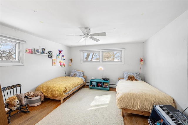 bedroom with baseboard heating, hardwood / wood-style floors, and multiple windows