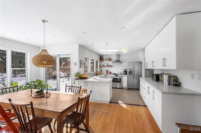 kitchen with appliances with stainless steel finishes, pendant lighting, sink, white cabinets, and wall chimney range hood