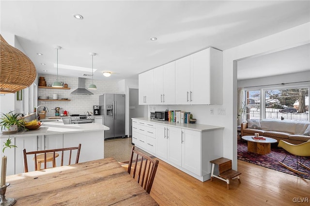 kitchen featuring appliances with stainless steel finishes, kitchen peninsula, white cabinets, and wall chimney exhaust hood