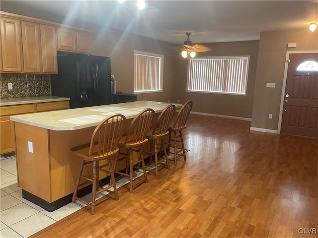 kitchen with black fridge, a center island, light hardwood / wood-style floors, and decorative backsplash