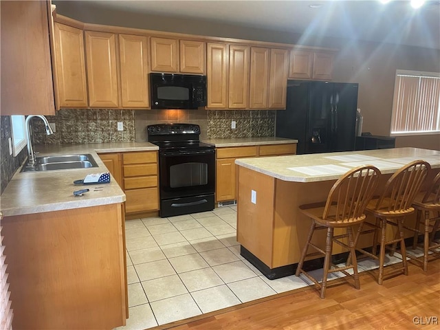 kitchen with sink, a center island, a kitchen breakfast bar, decorative backsplash, and black appliances