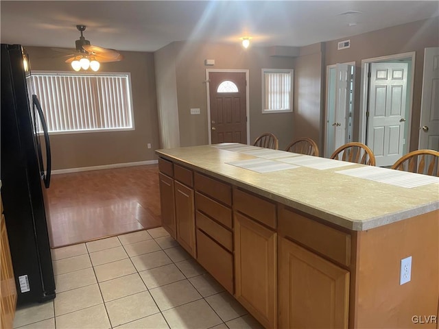 kitchen with light tile patterned flooring, a center island, black refrigerator, and ceiling fan