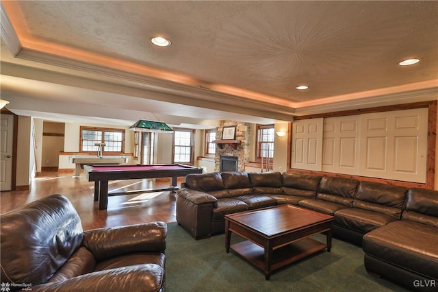 living room featuring billiards, ornamental molding, a stone fireplace, and a raised ceiling