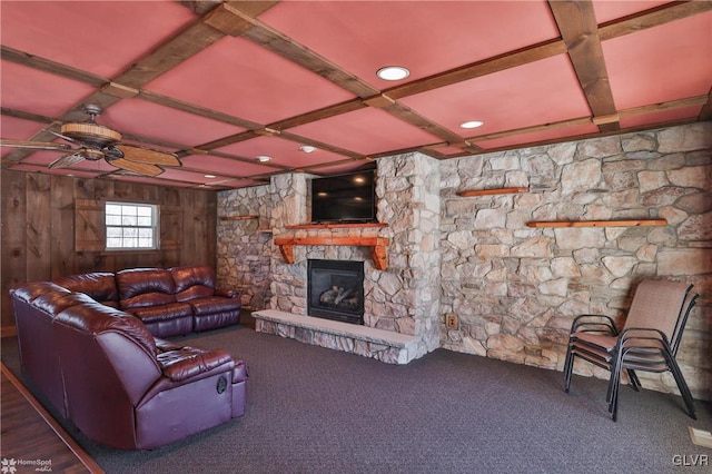 living room featuring ceiling fan, coffered ceiling, carpet floors, a stone fireplace, and wood walls