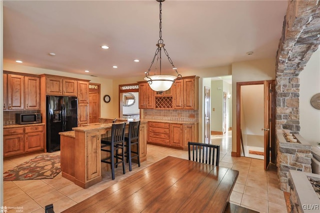 kitchen with pendant lighting, backsplash, a kitchen bar, a center island, and black fridge with ice dispenser