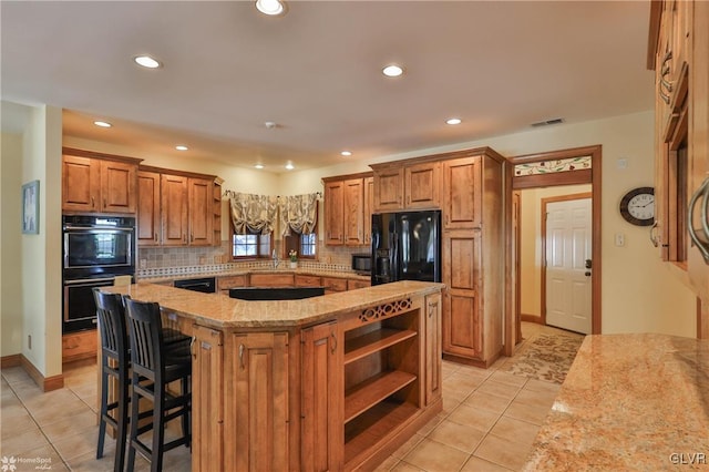 kitchen with light tile patterned flooring, a kitchen island, light stone countertops, decorative backsplash, and black appliances