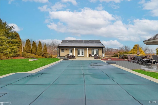 rear view of house featuring a lawn, a swimming pool side deck, a patio, solar panels, and french doors