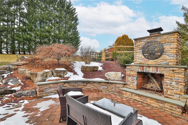 snow covered patio featuring an outdoor stone fireplace