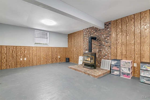 unfurnished living room with beam ceiling, concrete flooring, a wood stove, and wood walls