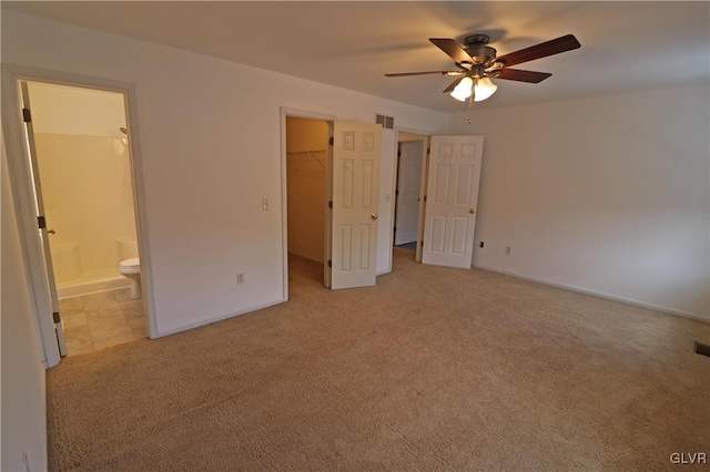 unfurnished bedroom with ensuite bathroom, a spacious closet, light carpet, a closet, and ceiling fan