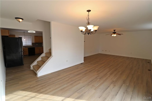 empty room with ceiling fan with notable chandelier and light hardwood / wood-style flooring