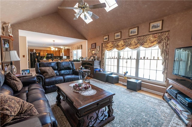 living room featuring ceiling fan with notable chandelier, high vaulted ceiling, and a skylight