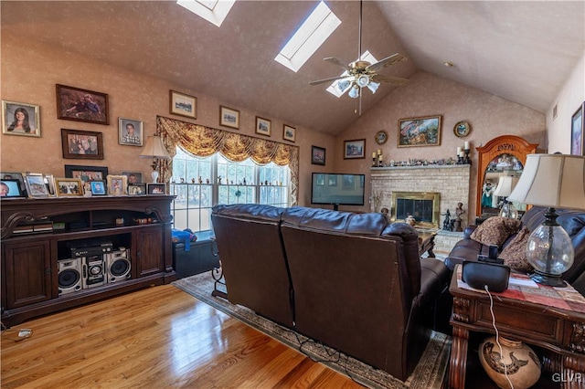 living room featuring light hardwood / wood-style flooring, ceiling fan, a skylight, high vaulted ceiling, and a fireplace