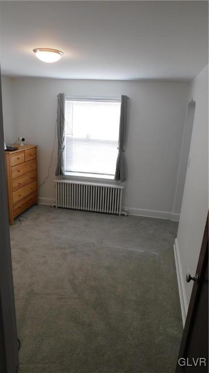 unfurnished bedroom featuring radiator and dark carpet