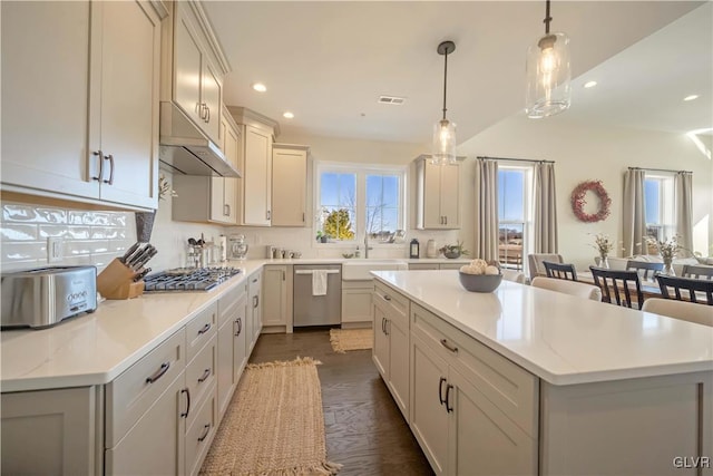 kitchen with appliances with stainless steel finishes, decorative light fixtures, sink, a center island, and light stone countertops