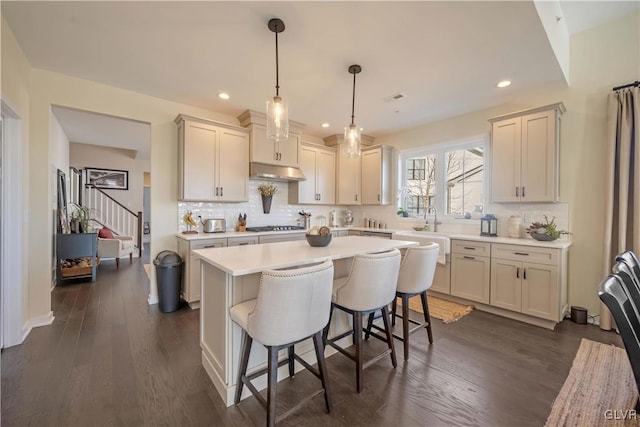 kitchen featuring dark hardwood / wood-style floors, stainless steel gas stovetop, backsplash, hanging light fixtures, and a center island