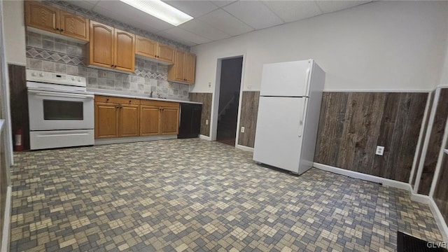 kitchen featuring white appliances, sink, wooden walls, and a paneled ceiling