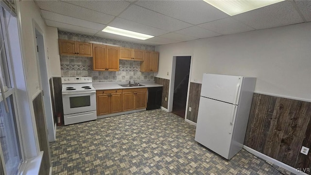 kitchen featuring white appliances, wooden walls, sink, and a drop ceiling