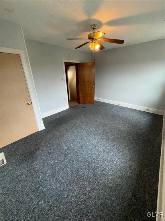 unfurnished bedroom featuring ceiling fan, a textured ceiling, and dark carpet