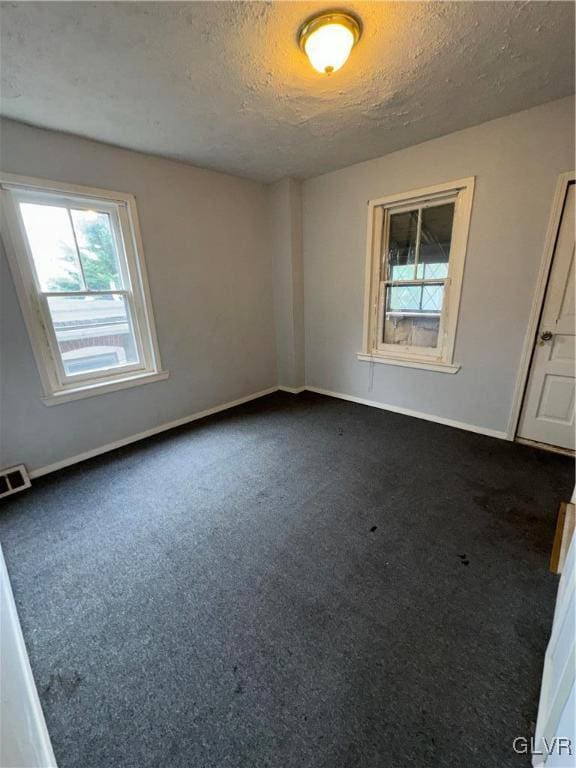 unfurnished room featuring a textured ceiling and dark carpet