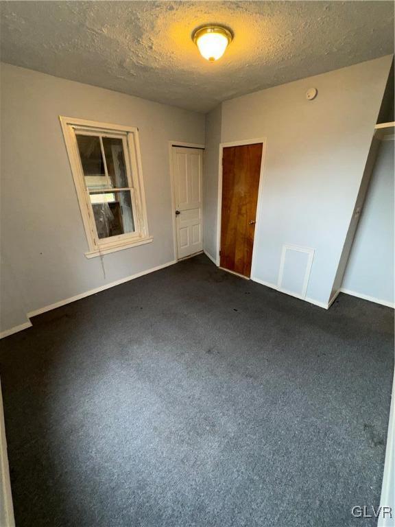 unfurnished bedroom with dark carpet, a closet, and a textured ceiling