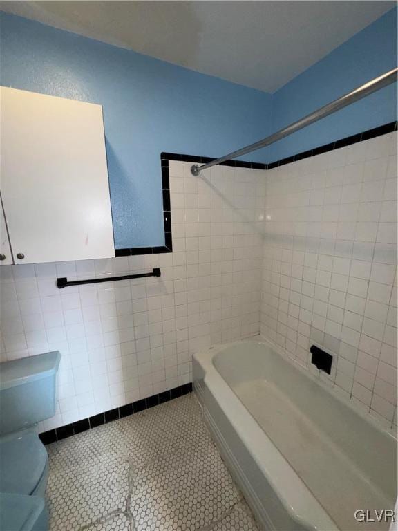 bathroom with tiled shower / bath, toilet, tile patterned flooring, and tile walls