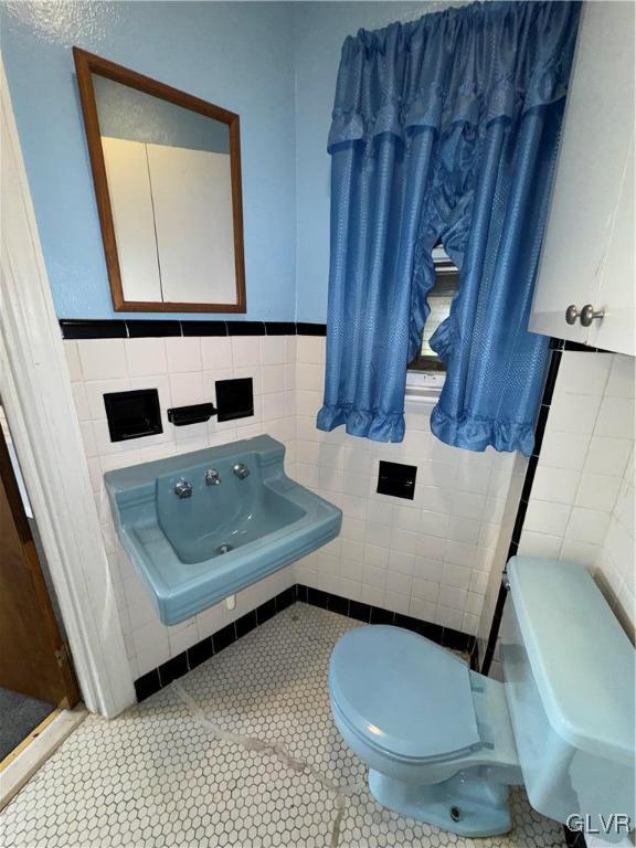 bathroom featuring tile patterned floors, toilet, sink, and tile walls