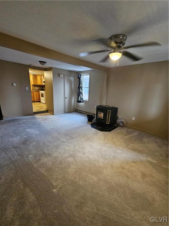 interior space with a textured ceiling, light carpet, baseboard heating, a wood stove, and ceiling fan